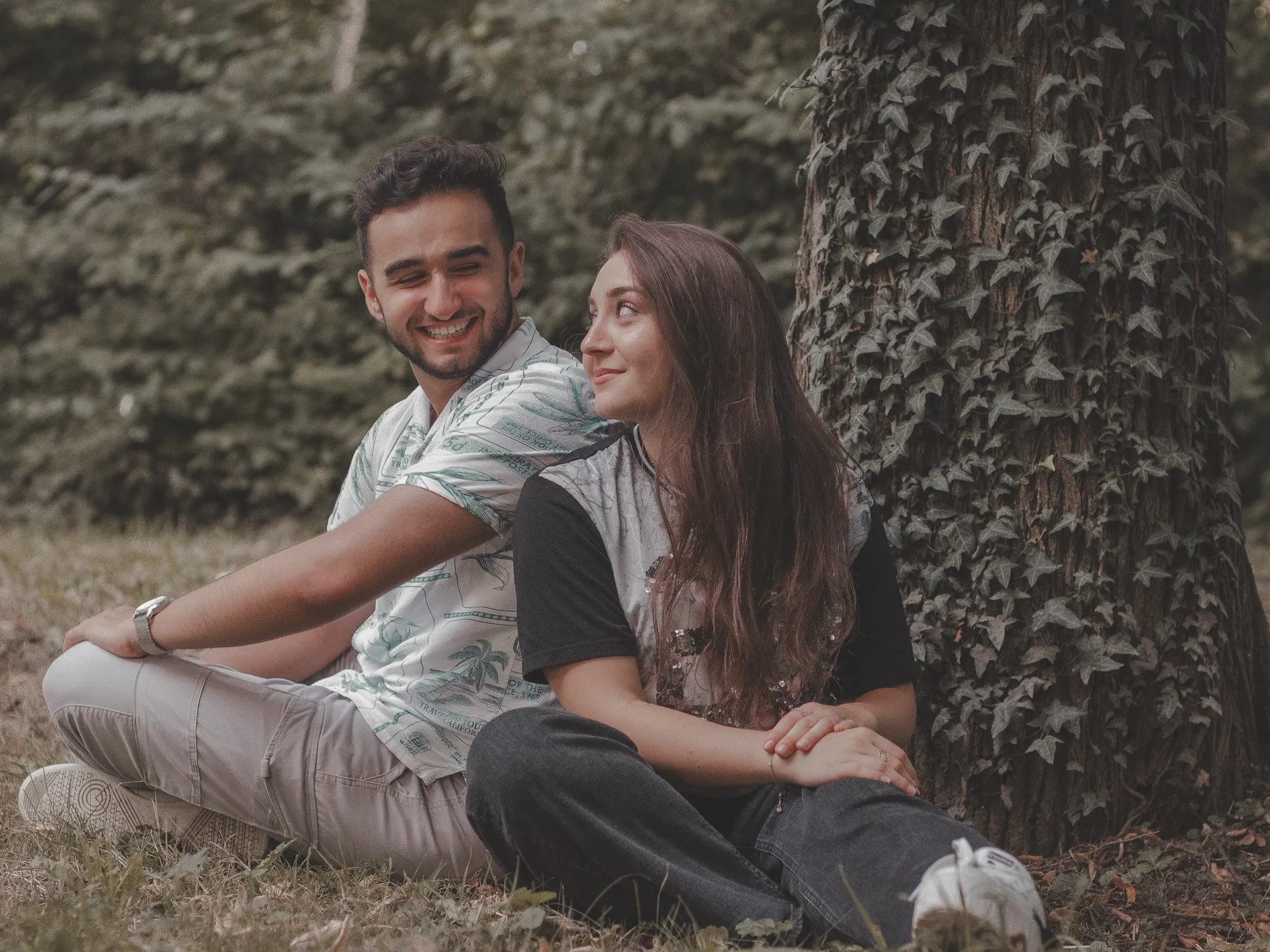 Paar sitzt lachend Rücken an Rücken im Wald, natürlicher Moment