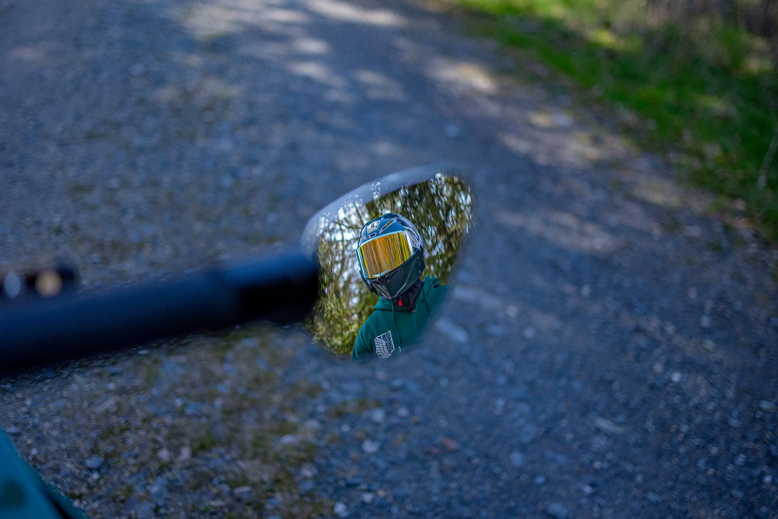 Motorradfahrer im Rückspiegel auf Schotterweg im Wald